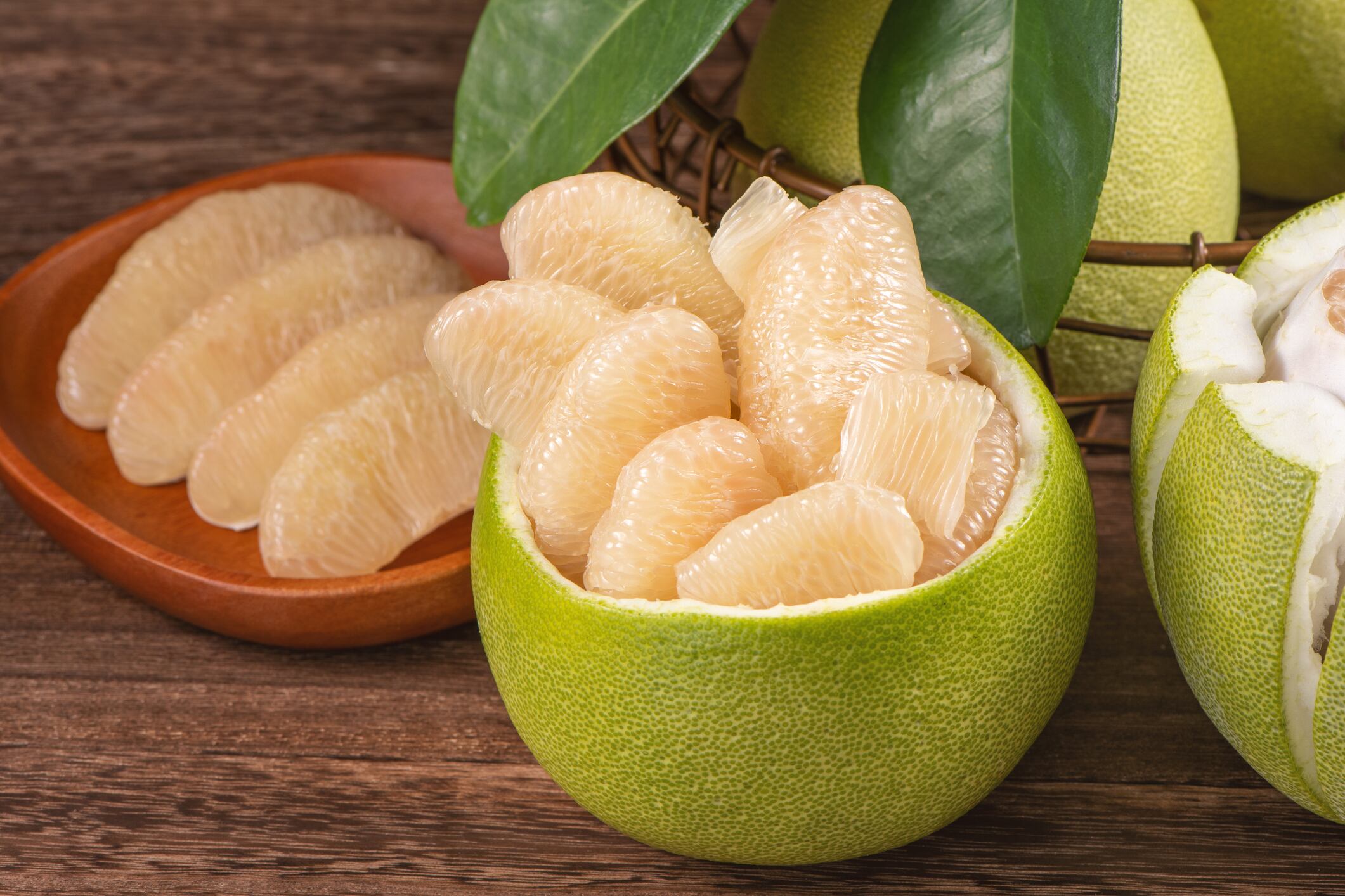 Fresh peeled pomelo, grapefruit, shaddock with green leaves on dark wooden plank table.